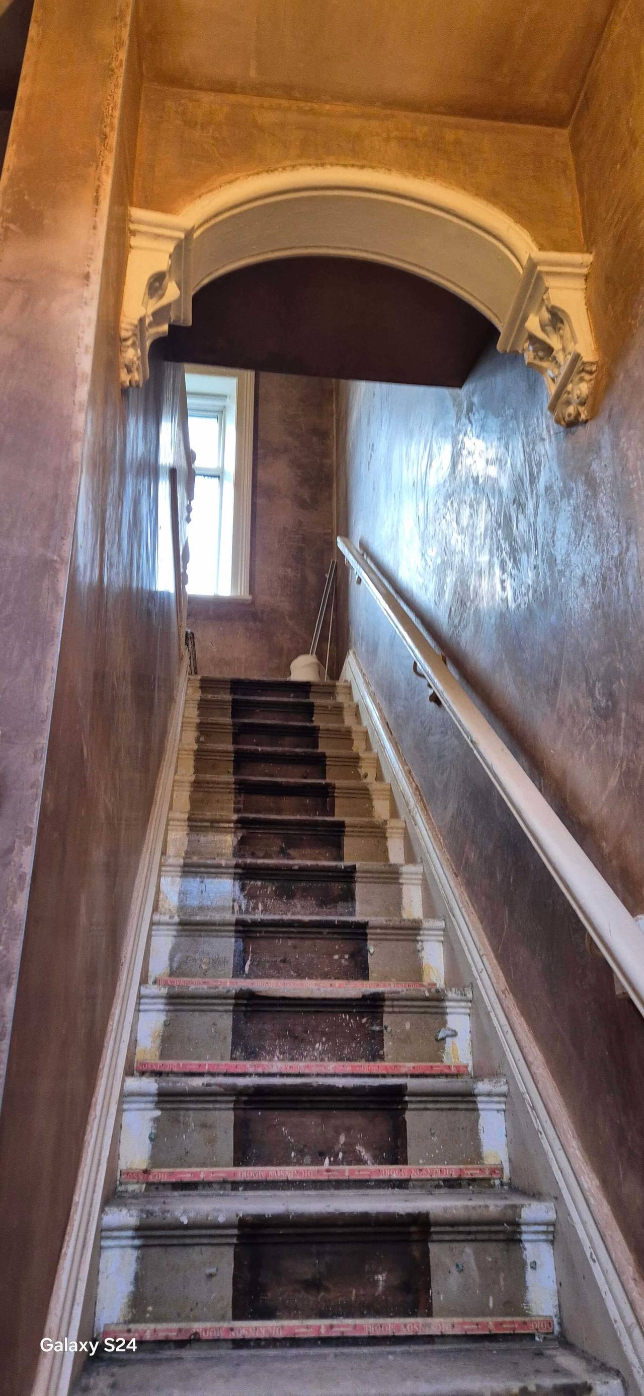 Freshly plastered stairwell with a restored ornate plaster archway and corbels above stripped stair treads