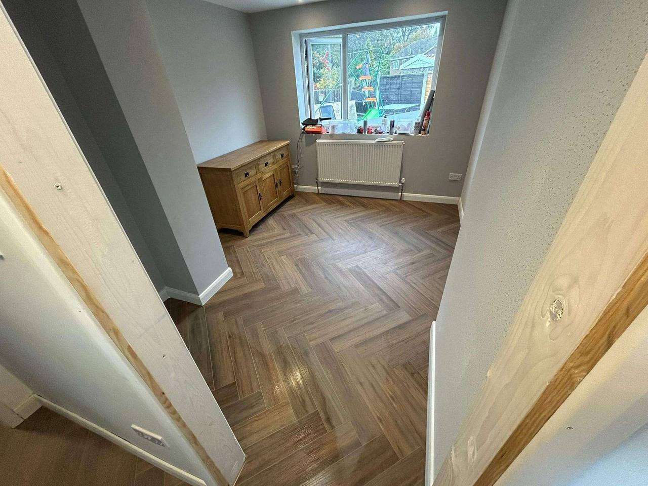 Freshly finished room with herringbone wood-effect flooring, pale grey walls and a new radiator beneath the window
