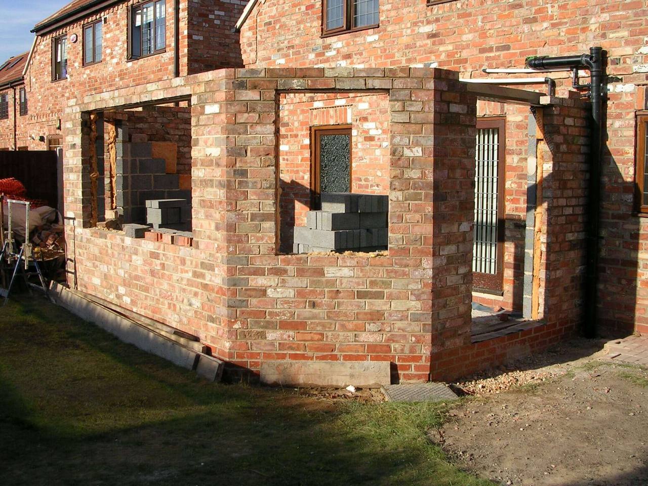Single-storey reclaimed-brick rear extension under construction, with window and door openings formed beside the main house